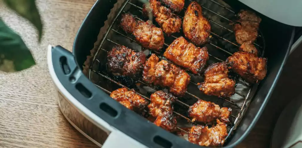 Browned, crisp chicken pieces cooked in an open air fryer basket on a wooden table