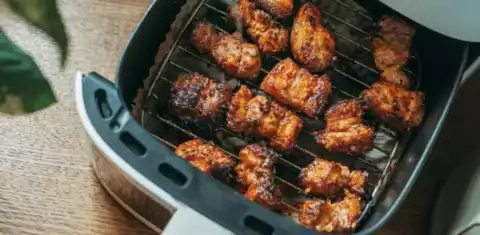 Browned, crisp chicken pieces cooked in an open air fryer basket on a wooden table
